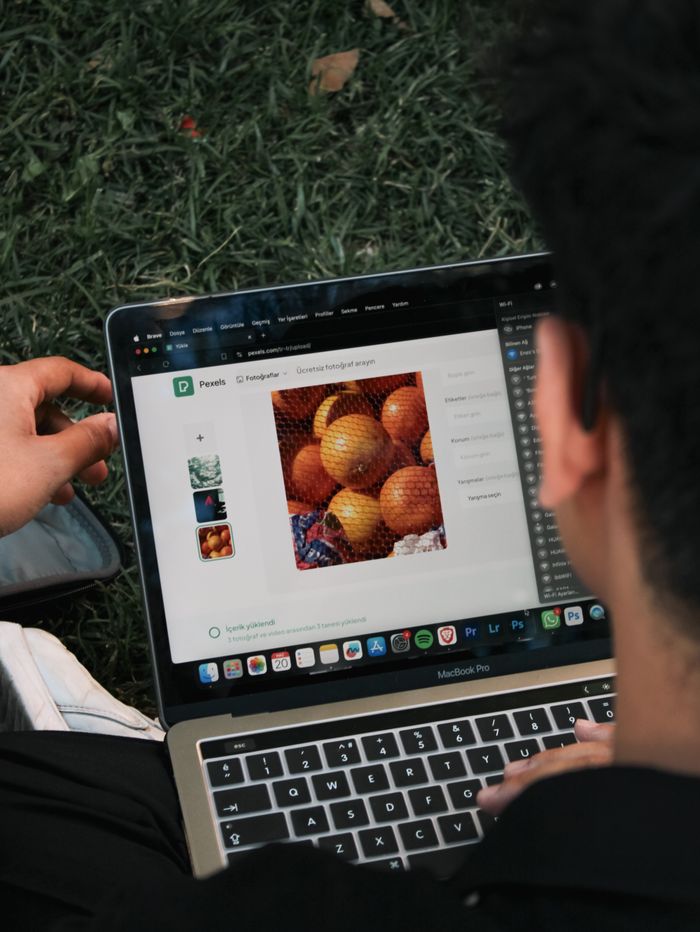 Un homme retouche l’image d’un fruit sur un MacBook Pro en étant assis dehors sur l’herbe.